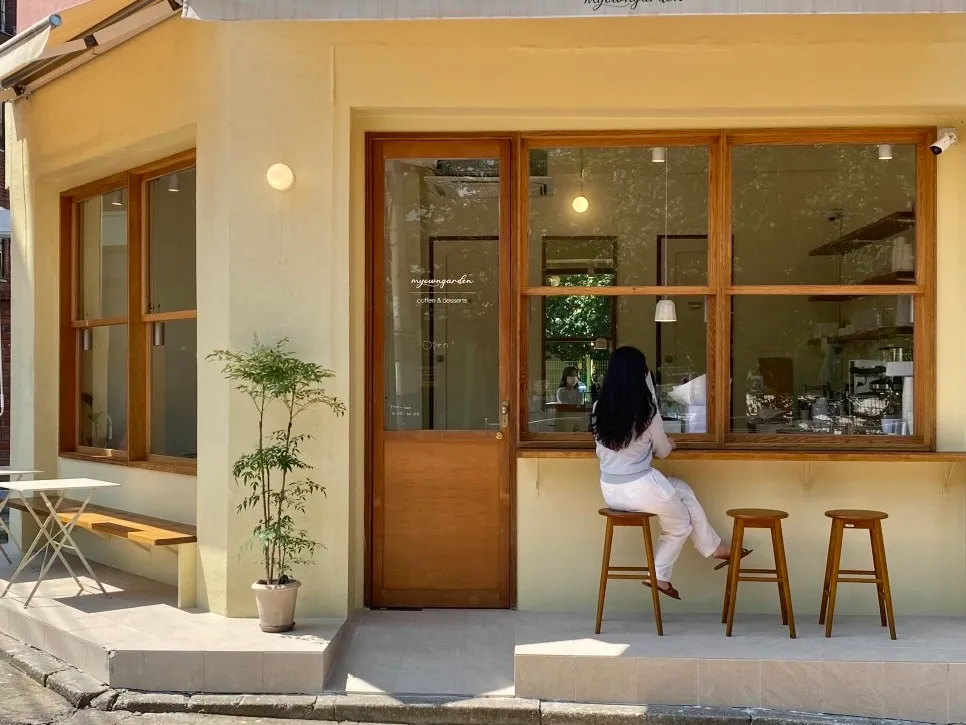 마이오운가든 카페 노란 외벽과 원목 창틀 아래 스툴 세 개가 나란히 놓여 있다